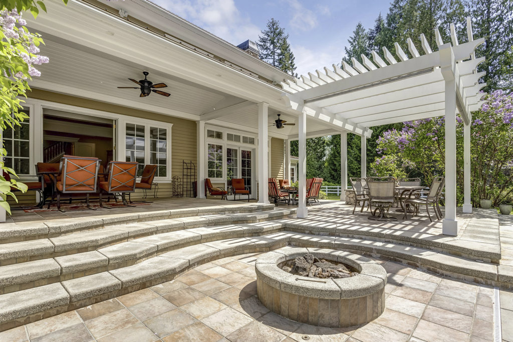 Lovely outdoor deck patio space with white pergola, fire pit in the backyard of a luxury house.