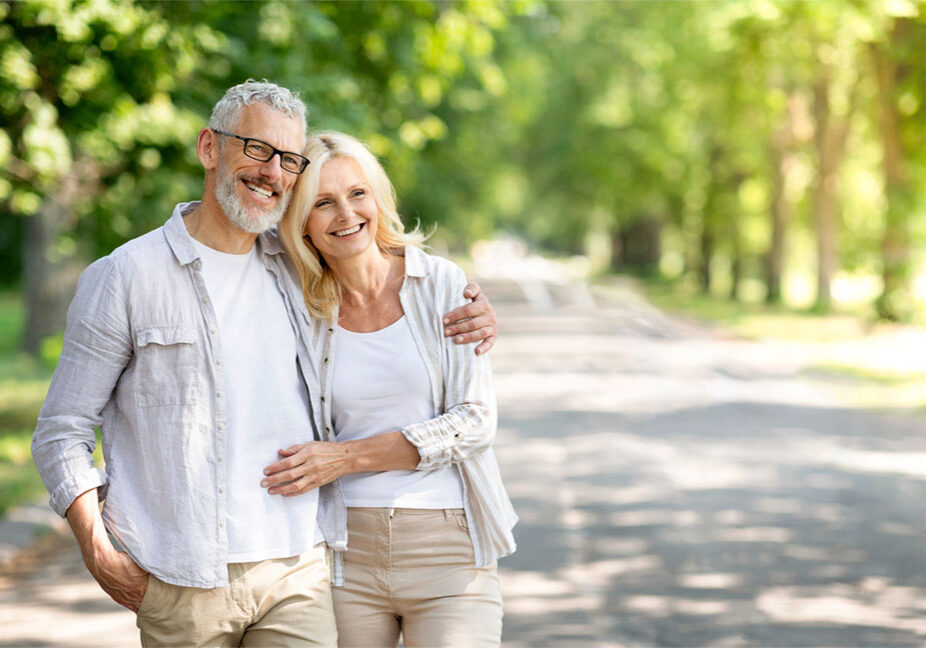 Beautiful mature spouses hugging outdoors while walking in summer park, happy senior couple embracing and looking away, older husband and wife enjoying time together, having romantic date outside